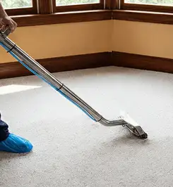 Steam carpet cleaning technician using a hot-water extraction wand on a residential carpet, wearing blue protective shoe covers Madison, WI.